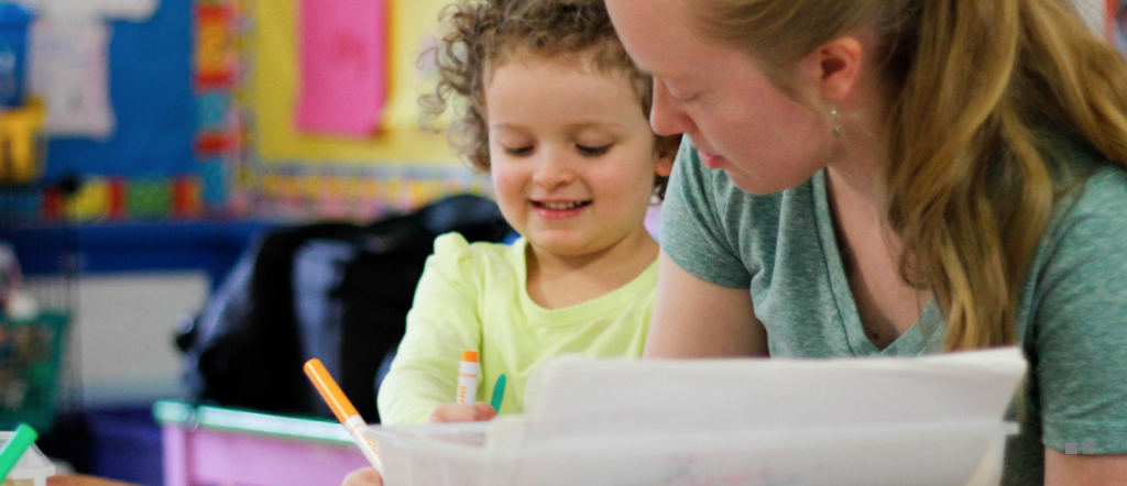 Teacher and student in a classroom, drawing with markers. 