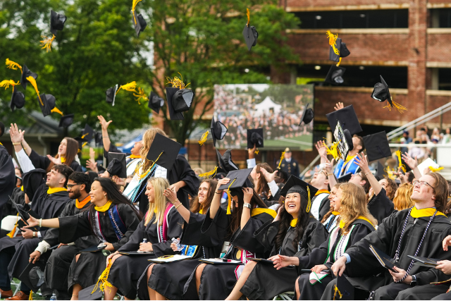 students in the school of nursing and health sciences toss their graduation caps in lions stadium